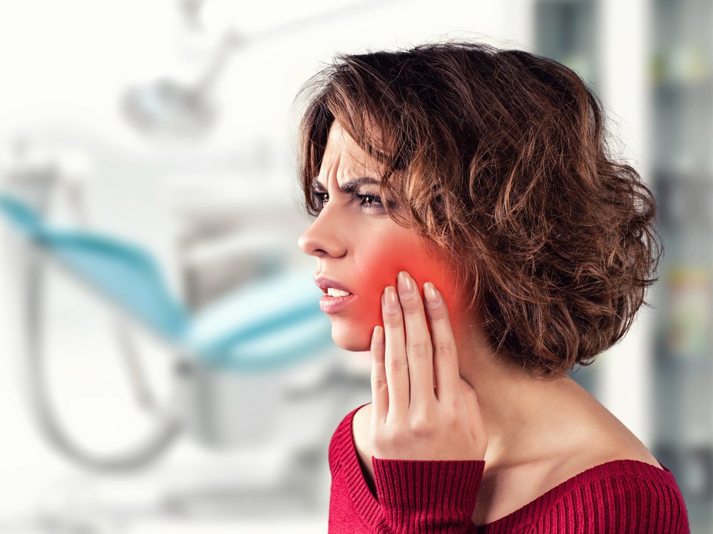 Woman holding the side of her face due to tooth pain and looking for an emergency dentist in Newport Beach, CA.